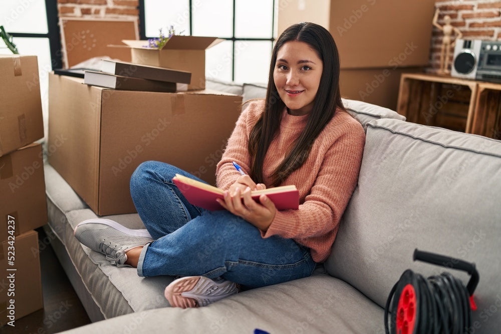 Young hispanic woman writing on book sitting on sofa at new home Young hispanic woman writing on book sitting on sofa at new home