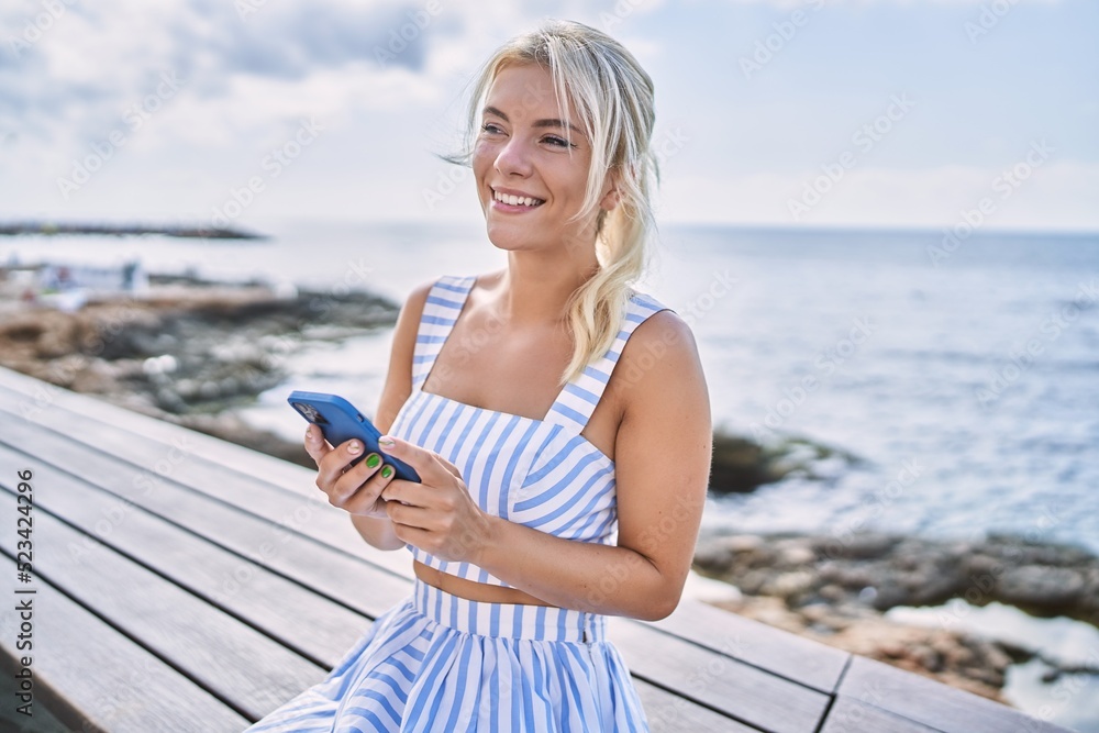 Young blonde girl using smartphone sitting on the bench at the beach.