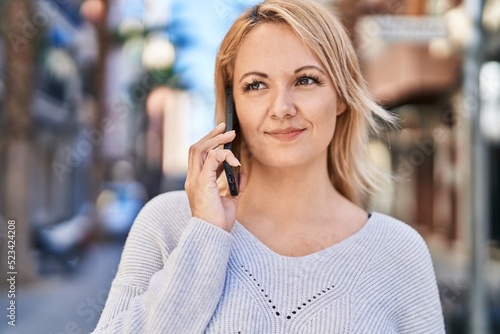 Young blonde woman smiling confident talking on the smartphone at street