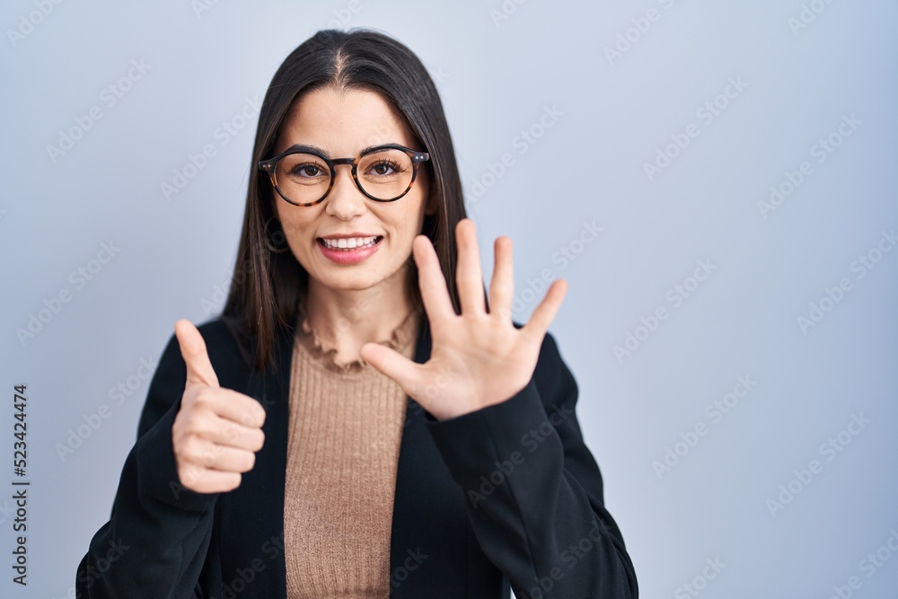Young brunette woman standing over blue background showing and pointing up with fingers number six while smiling confident and happy. Young brunette woman standing over blue background showing and pointing up with fingers number six while smiling confident and happy.