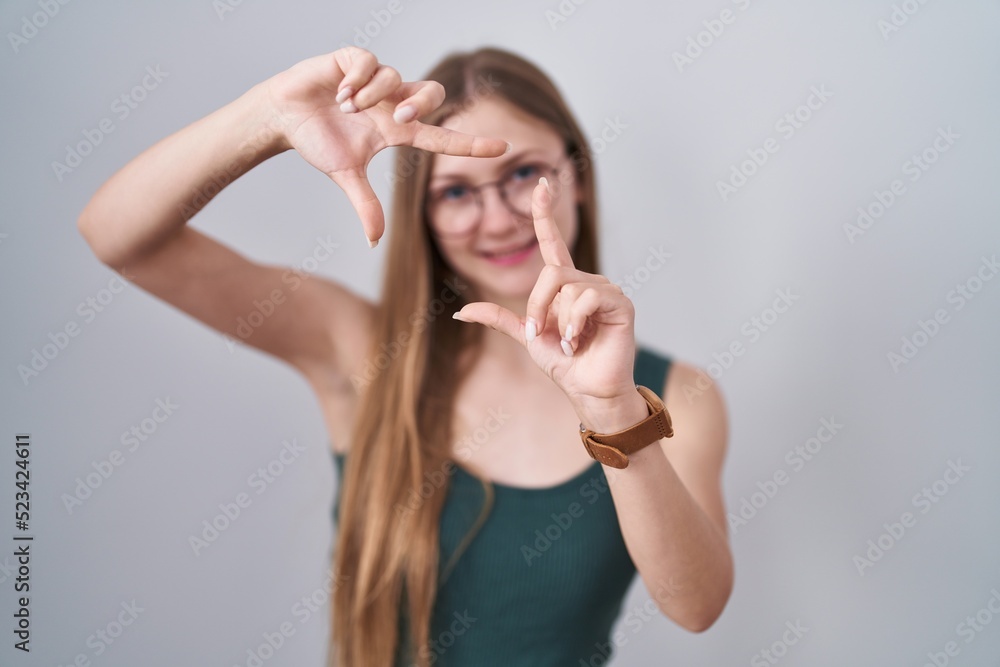 Fototapeta premium Young caucasian woman standing over white background smiling making frame with hands and fingers with happy face. creativity and photography concept.