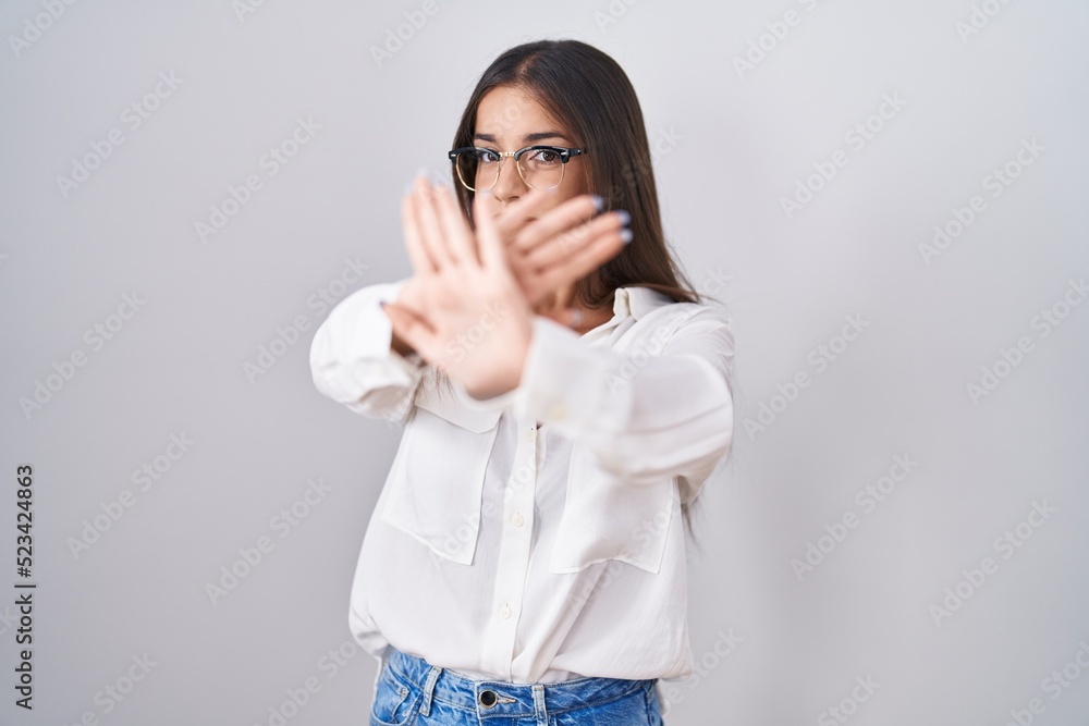 Young brunette woman wearing glasses rejection expression crossing arms and palms doing negative sign, angry face Young brunette woman wearing glasses rejection expression crossing arms and palms doing negative sign, angry face