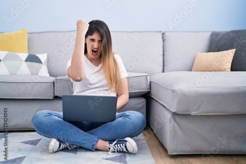 Free Download Young brunette woman sitting on the floor at home using laptop annoyed and frustrated shouting with anger, yelling crazy with anger and hand raised - GFXLoad