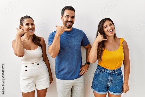 Group of young hispanic people standing over isolated background smiling doing phone gesture with hand and fingers like talking on the telephone. communicating concepts.