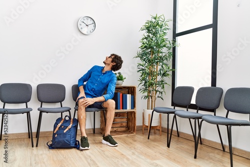 Young hispanic man sitting on chair looking clock at waiting room