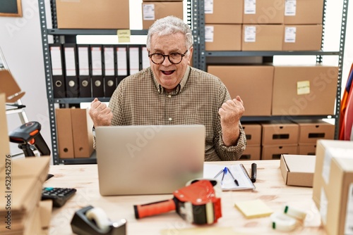 Senior caucasian man working at small business ecommerce with laptop celebrating surprised and amazed for success with arms raised and open eyes. winner concept.