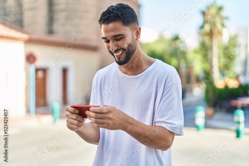 Young arab man smiling confident watching video on smartphone at street