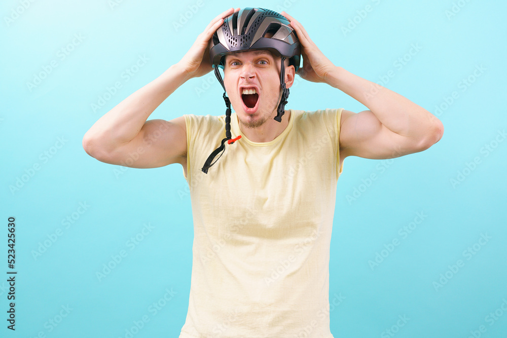 A crazy man wearing a bicycle helmet holding his head on a blue background. Object. Outdoor. Person. Protection. Road. Safety. Security. Service. Shield. Sport. Sportswear. Standing. Transportation A crazy man wearing a bicycle helmet holding his head on a blue background. Object. Outdoor. Person. Protection. Road. Safety. Security. Service. Shield. Sport. Sportswear. Standing. Transportation