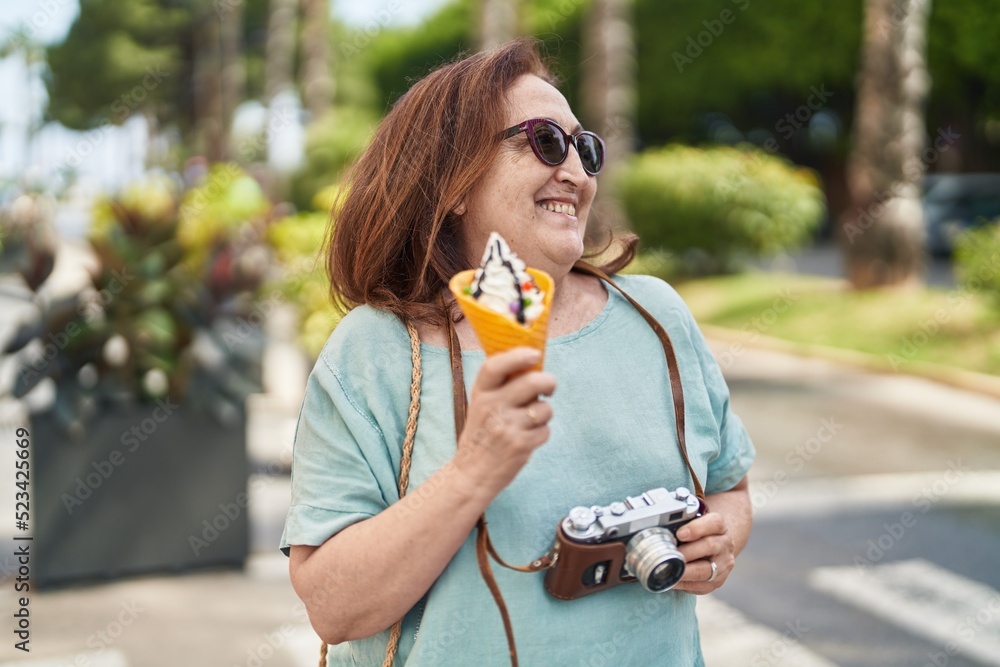 Senior woman tourist holding camera eating ice cream at street