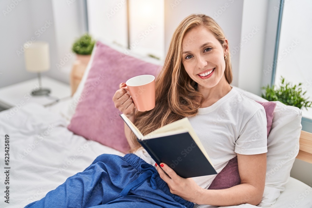 Young blonde woman drinking cup of coffee reading book at bedroom Young blonde woman drinking cup of coffee reading book at bedroom