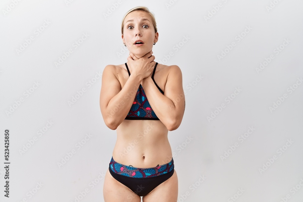 Naklejka premium Young blonde woman wearing sporty bikini over isolated background shouting suffocate because painful strangle. health problem. asphyxiate and suicide concept.