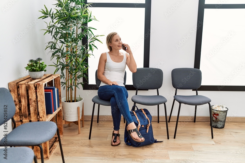 Young caucasian woman talking on the smartphone sitting on chair at waiting room Young caucasian woman talking on the smartphone sitting on chair at waiting room
