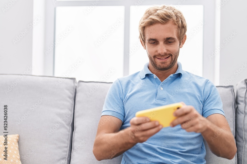 Young man using smartphone sitting on sofa at home Young man using smartphone sitting on sofa at home