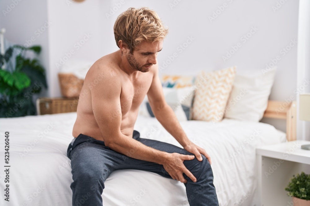 Young man suffering for knee injury sitting on bed at bedroom Young man suffering for knee injury sitting on bed at bedroom