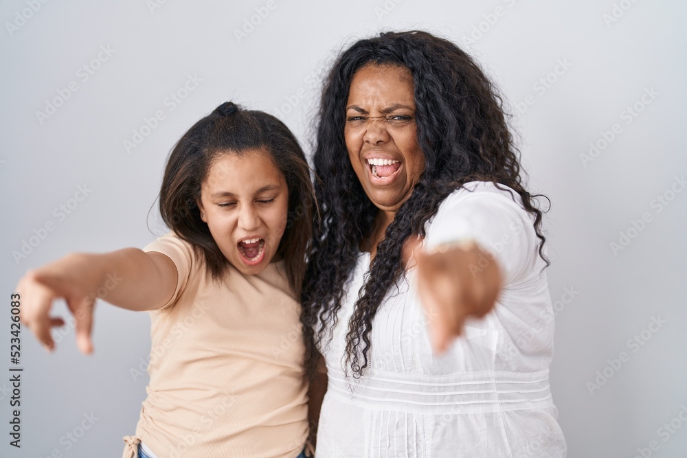 Mother and young daughter standing over white background pointing displeased and frustrated to the camera, angry and furious with you Mother and young daughter standing over white background pointing displeased and frustrated to the camera, angry and furious with you