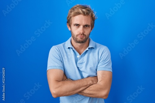Caucasian man standing over blue background skeptic and nervous, disapproving expression on face with crossed arms. negative person.