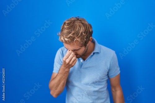 Caucasian man standing over blue background tired rubbing nose and eyes feeling fatigue and headache. stress and frustration concept.