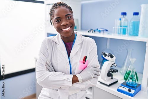 African american woman wearing scientist uniform standing with arms crossed gesture at laboratory