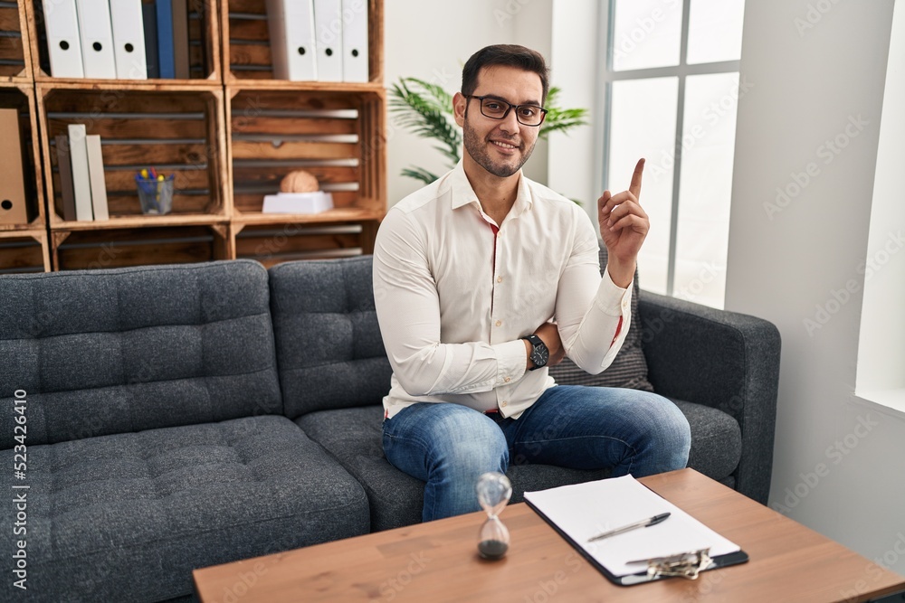 Young hispanic man with beard working at consultation office with a big smile on face, pointing with hand finger to the side looking at the camera. Young hispanic man with beard working at consultation office with a big smile on face, pointing with hand finger to the side looking at the camera.