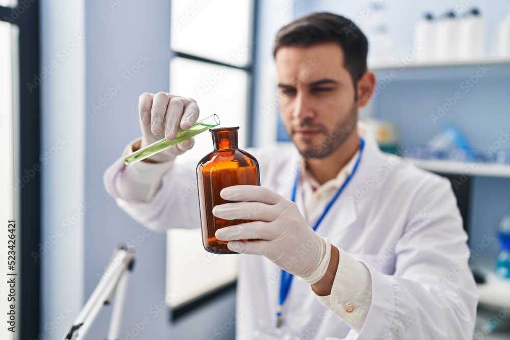 Young hispanic man scientist pouring liquid on bottle at laboratory Young hispanic man scientist pouring liquid on bottle at laboratory