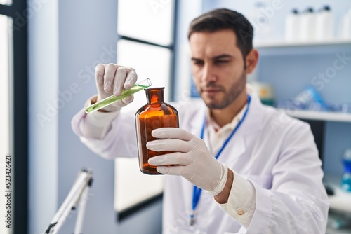 Young hispanic man scientist pouring liquid on bottle at laboratory