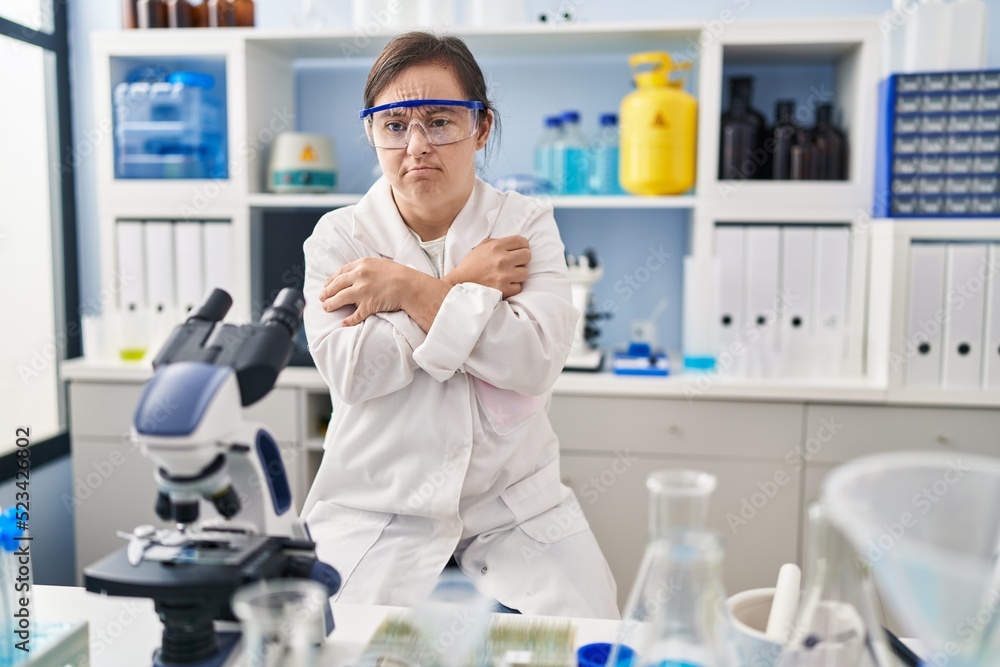 Fototapeta premium Hispanic girl with down syndrome working at scientist laboratory shaking and freezing for winter cold with sad and shock expression on face