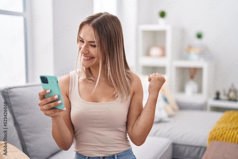 Blonde caucasian woman using smartphone typing message sitting on the sofa screaming proud, celebrating victory and success very excited with raised arms Blonde caucasian woman using smartphone typing message sitting on the sofa screaming proud, celebrating victory and success very excited with raised arms