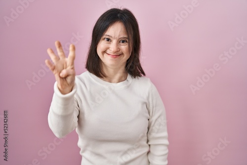 Woman with down syndrome standing over pink background showing and pointing up with fingers number four while smiling confident and happy.
