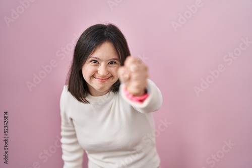 Woman with down syndrome standing over pink background angry and mad raising fist frustrated and furious while shouting with anger. rage and aggressive concept. © Krakenimages.com