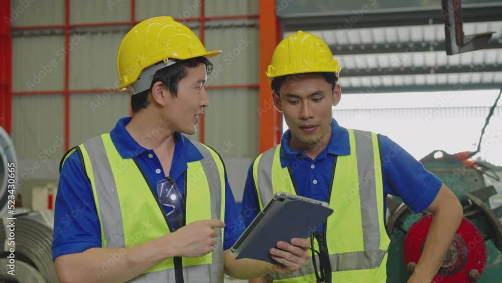 Two workers wearing safety uniforms and hard hats using a digital tablet in the factory. Asian men are 23, 27-year-old and working, professional industrial. Slow Motion Two workers wearing safety uniforms and hard hats using a digital tablet in the factory. Asian men are 23, 27-year-old and working, professional industrial. Slow Motion