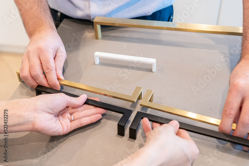 Male and female hands placing kitchen cabinet handles in configuration to make a selection for their home interior decor.