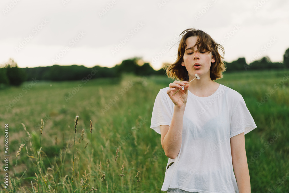 Beautiful teenager girl on the field in green grass and blowing dandelion. Outdoors. Enjoy Nature. Healthy Smiling Girl on summer lawn. Allergy free concept. Beautiful teenager girl on the field in green grass and blowing dandelion. Outdoors. Enjoy Nature. Healthy Smiling Girl on summer lawn. Allergy free concept.