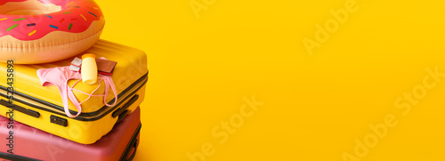Suitcases and beach accessories on yellow background with space for text