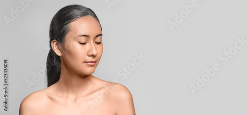 Asian woman with graying hair on light background with space for text