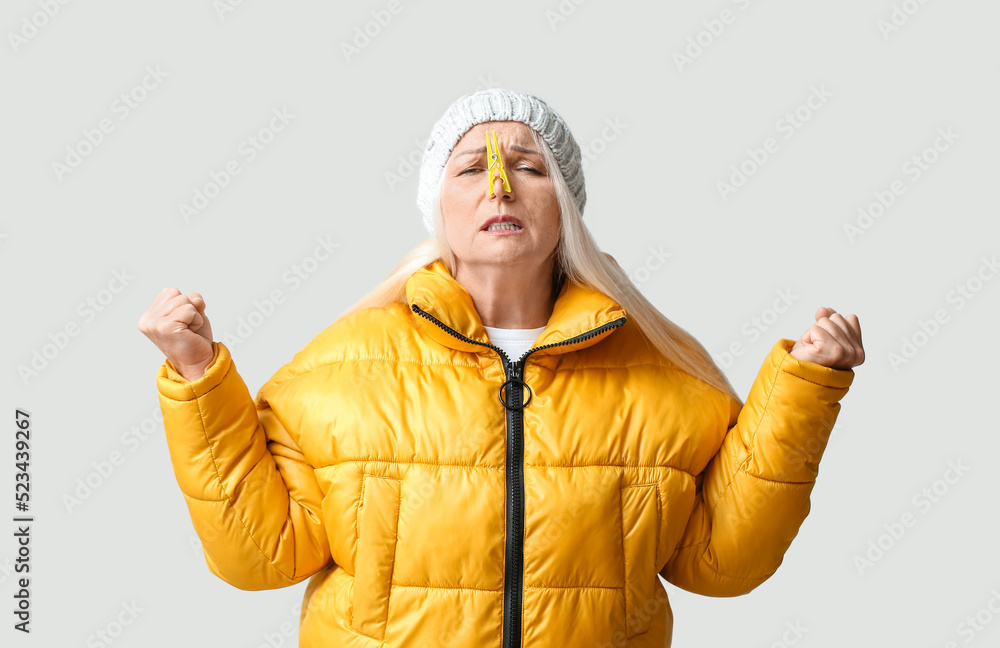 Stressed mature woman with clothespin on light background. Stuffy nose concept Stressed mature woman with clothespin on light background. Stuffy nose concept