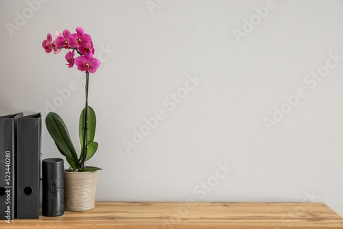 Beautiful orchid flower and folders on table near white wall