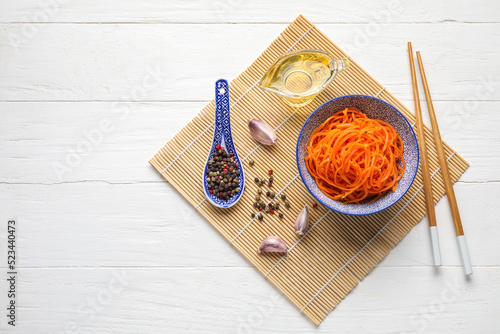 Mat with bowl of carrot salad and ingredients on white wooden background