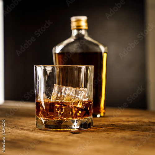 Wiskey in a glass with the ice cubes on the reflective black surface. Bar drinking menu