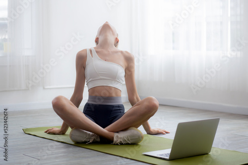 Young woman doing yoga with sitting and stretch muscles back and neck on mat at home, female training practicing workout with exercise while watching laptop computer for bodycare, sport concept.
