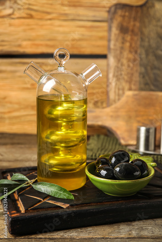 Board with bottle of oil and olives on wooden table