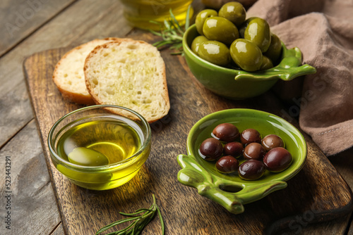 Board with bowls of oil and olives on wooden table, closeup