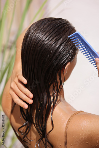 Hair Beauty. Closeup Of Beautiful Woman Hairbrushing With Comb At the Street. Young Female Model Putting Refreshing Mask On Long Wet Hair With Wooden Comb  photo