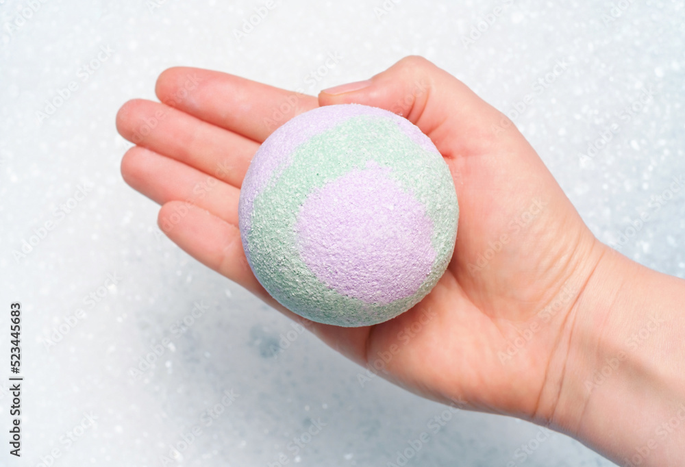 Hand hold a bath bomb against the background of foam close-up. Hand hold a bath bomb against the background of foam close-up.