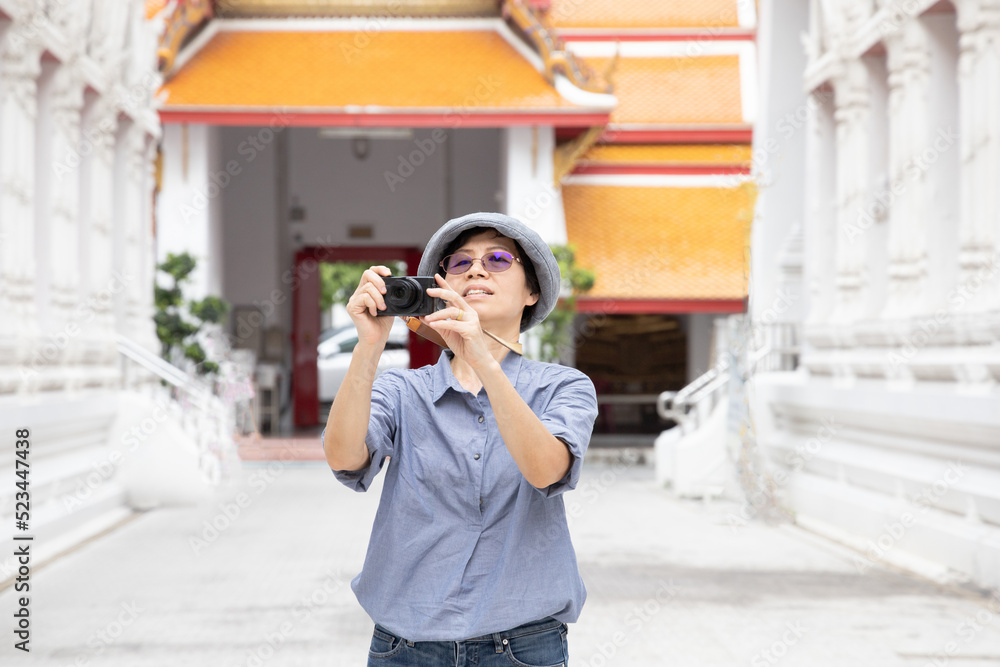 Asian senior woman tourist taking photo by camera in Thai temple