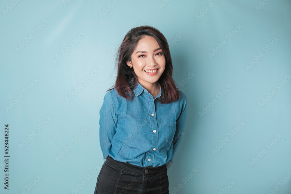 Fototapeta premium A portrait of a happy Asian woman is smiling and wearing a blue shirt isolated by a blue background