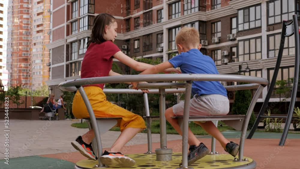 Two cheerful children are spinning on a carousel on the playground in the yard. Two cheerful children are spinning on a carousel on the playground in the yard.