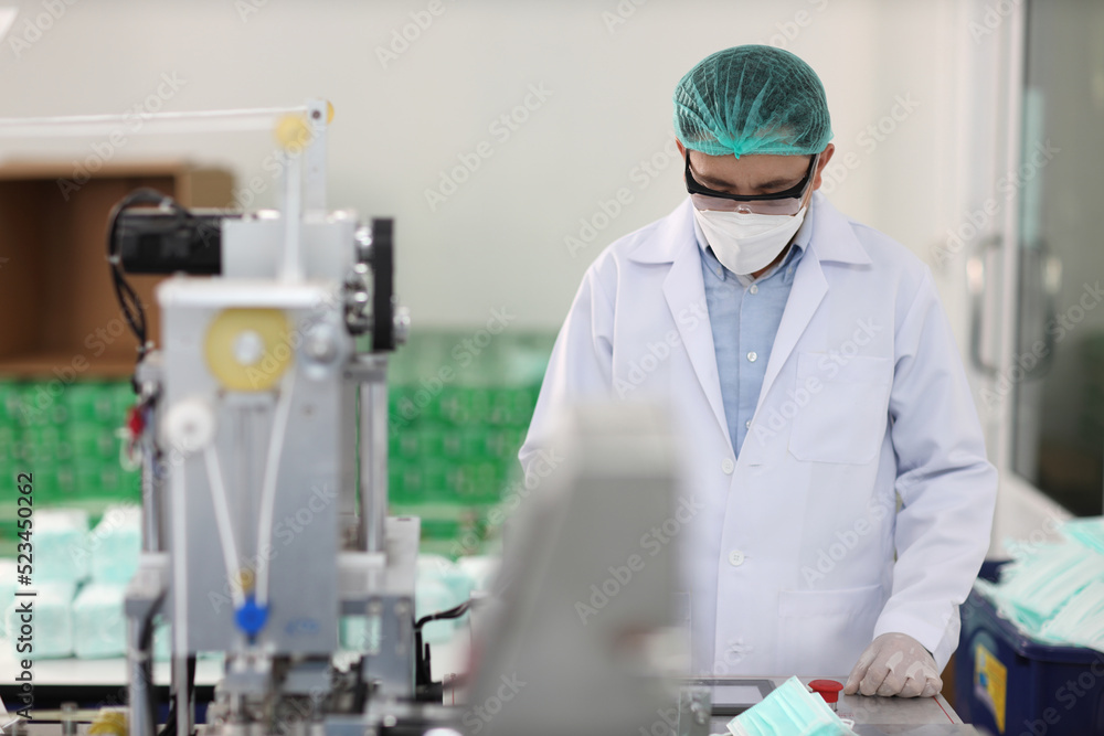 Naklejka premium Worker in personal protective equipment or PPE inspecting quality of mask and medical face mask production line in factory, manufacturing industry and factory concept.