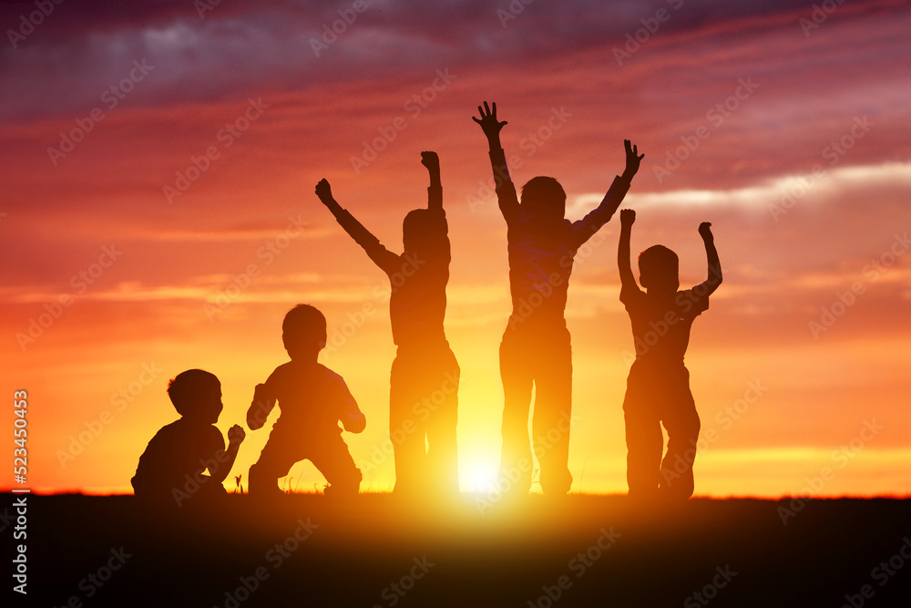 Children's happy silhouettes at sunset. Group of funny kids are jumping in the meadow on a summer evening.