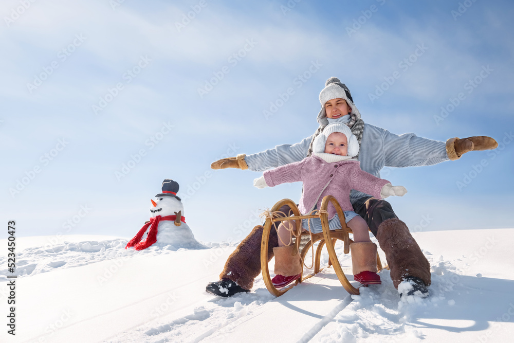 Children are sledding down the hill. Happy boy and girl in rustic style have fun on winter holidays outdoors.