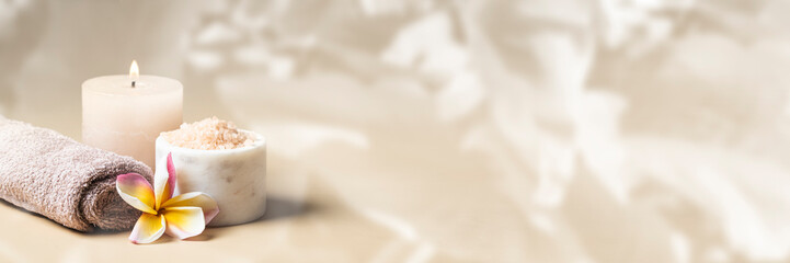 Foto auf Acrylglas Massagesalon Beauty Spa salon banner. Burning candle, towel with frangipani flower and salt scrub on beige background with tropical leafe texture.  © vasanty